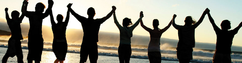 Line of young people standing on a beach holding hands at sunset