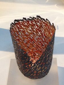 An image of a vessel formed from a discarded food can, with applied copper leaf and 23 carat red gold.